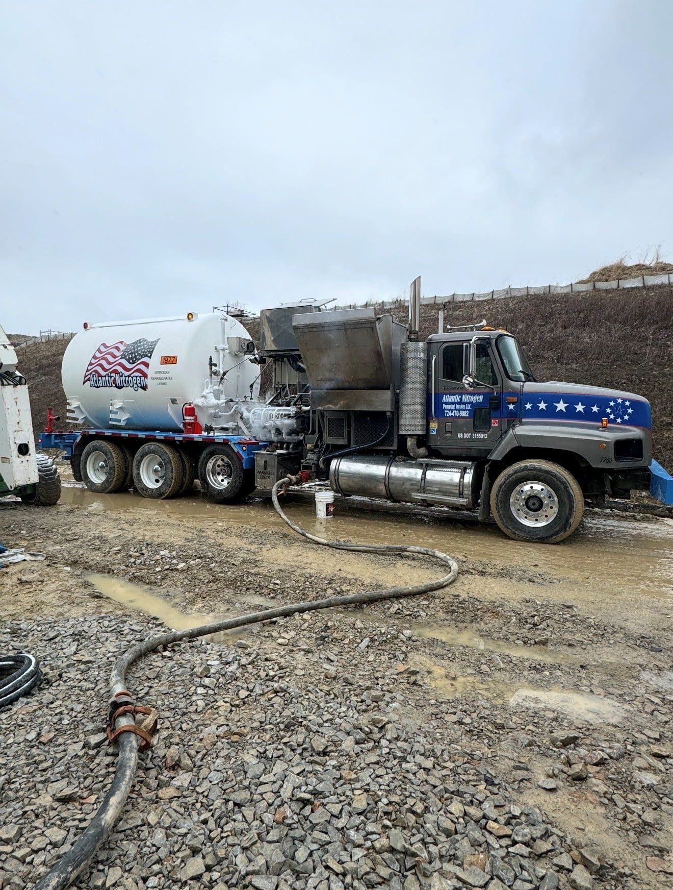 Cryogenic nitrogen pumper truck working on a gravel pad with a hose run out in the foreground